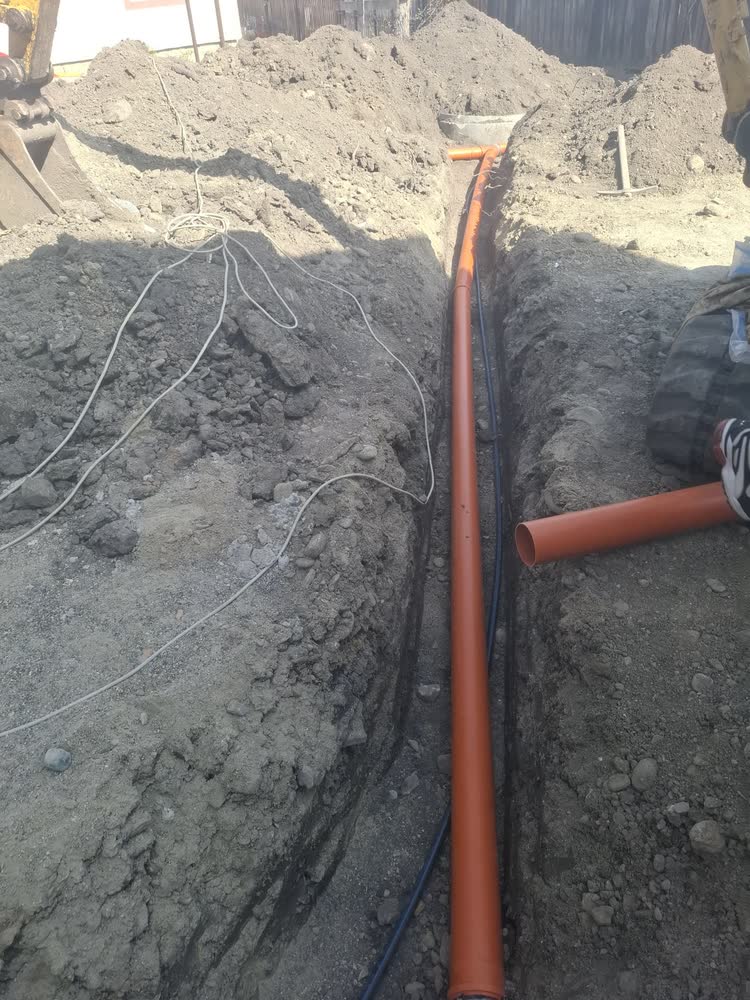 Șanț cu tub de canalizare și cabluri de curent, trase în aceeași săpătură.